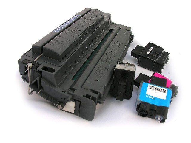 Une cartouche de toner laser noire volumineuse à côté de plusieurs petites cartouches d'encre jet d'encre de couleurs cyan et magenta, prêtes pour la collecte et le recyclage.