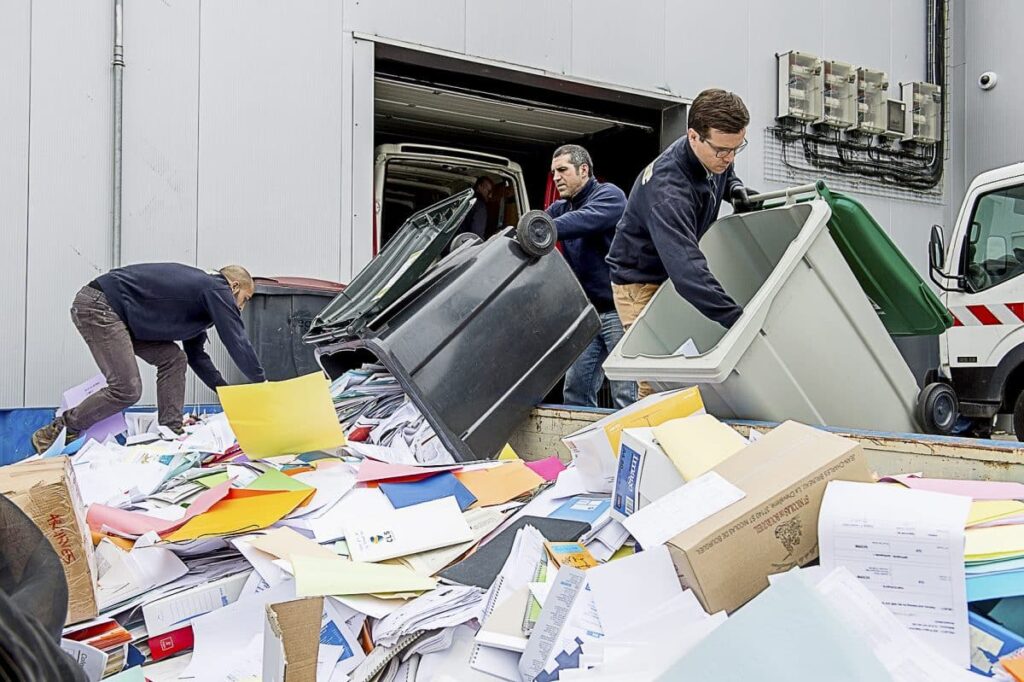 Employés procédant à la destruction sécurisée et au recyclage de documents papier confidentiels dans une entreprise, à l’aide de bacs et conteneurs dédiés à la gestion des déchets.